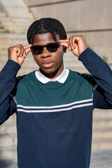 Young man adjusting his sunglasses while standing on steps in an urban environment, showcasing modern youth style and confidence