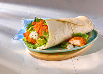 Wrap mit Salat fritteirtem Haehnchen und Remouladensauce mit hellblauer Serviette auf blauem Teller und Holzfond,