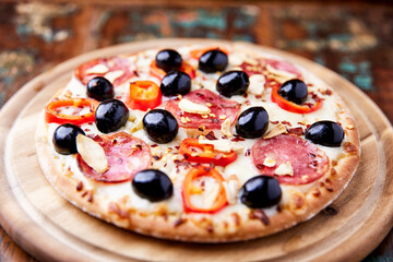Pizza with salami and mozzarella cheese, jalapeno pepper and black olives. Wooden background. Soft focus. Close up.	