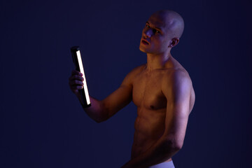 Intense man holding a light in a dark setting, showcasing dramatic shadows and vibrant contrast. A...