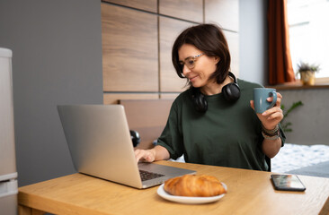 Freelance Girl Working At Home On A Computer While Having Breakfast In The Kitchen