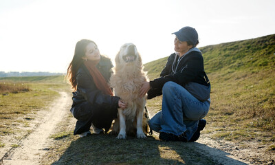 Girls Petting Adorable Golden Retriever Dog While Walking Outdoors At Sunset