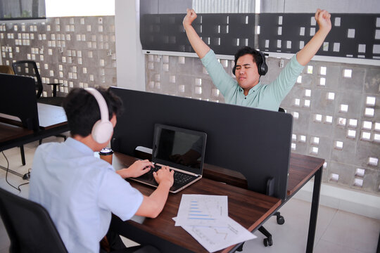 Office Workers In A Shared Workspace, One Stretching While Another Focuses On A Laptop - Powered by Adobe