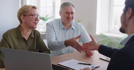 Happy smiling senior couple sitting at desk in office having consultation with male financial advisor about health insurance and shaking hands making deal. Investment in retirement concept. 4k video. - Powered by Adobe