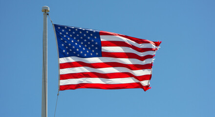 Fototapeta premium The American flag waving proudly against a clear, cloudless blue sky.