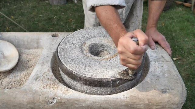 Man is grinding rye into wholemeal flour at quern. Life in medieval village.