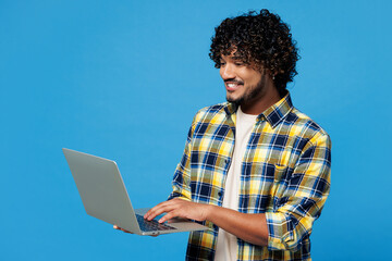 Side view young smiling happy IT Indian man he wear yellow checkered shirt casual clothes hold use...