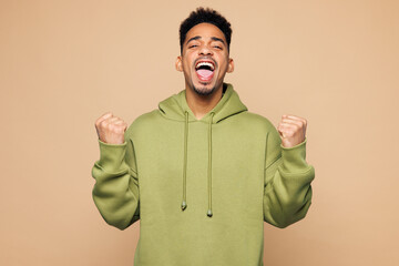 Young man of African American ethnicity wear green hoodie casual clothes doing winner gesture...