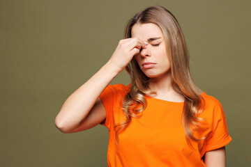 Young sad sick ill tired Caucasian woman she wearing orange t-shirt casual clothes keep eyes closed rub put hand on nose isolated on plain pastel green background studio portrait. Lifestyle concept.