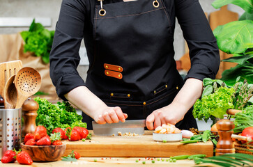 skilled chef in stylish black apron chops walnuts and fresh vegetables and fruits, creating a...