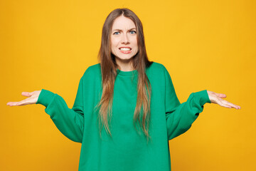 Young sad woman she wear green sweatshirt casual clothes spread hands shrugging shoulders looking...