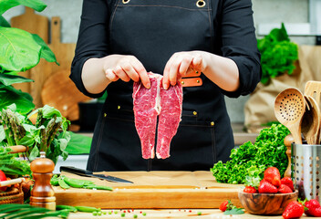 Chef cooking food in the kitchen. Cook hands holds separate fresh beef steak amidst vegetables on...