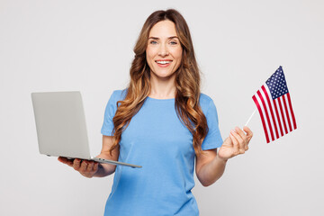 Young IT woman wearing blue t-shirt casual clothes hold American flag use work on laptop pc...