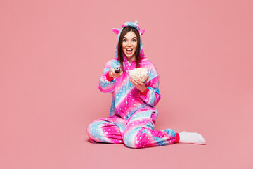 Full body young woman wear domestic costume with hoody and animal ears sit eat popcorn watch movie film switch channel isolated on plain pastel light pink background studio portrait Lifestyle concept