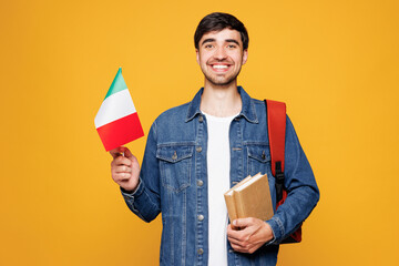 Naklejka na ściany i meble Young smiling clever fun English boy student wearing denim casual clothes backpack bag hold books Italian flag look camera isolated on plain yellow background. High school university college concept.