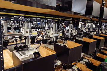 Automated machines line shelves in a workshop, working on intricate black objects. Industry,...