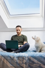 Man working from home with pet dog sitting on bed using laptop