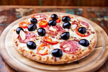 Pizza with salami and mozzarella cheese, jalapeno pepper and black olives. Wooden background. Soft focus. Close up.	
