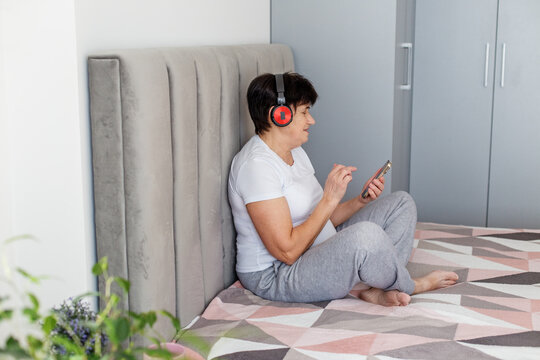 Senior woman using smartphone and headphones in bed