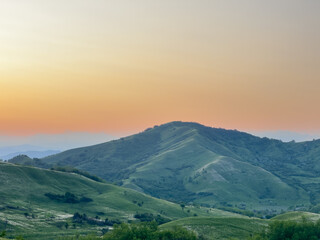 Obraz premium Buzău Green Hills Sunset. A serene landscape view captures rolling green hills in Buzău County, Romania, bathed in the warm hues of a sunset. 