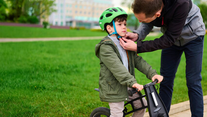 father adjusting child’s bicycle helmet, outdoors safety concept. parent ensures kid's protection...