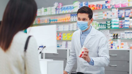 Female client choosing pills in pharmacy. Male pharmacist picking up medicine for woman. Man...