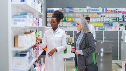 Woman pharmacist advising medicine to female client. African American druggist advising pills to...