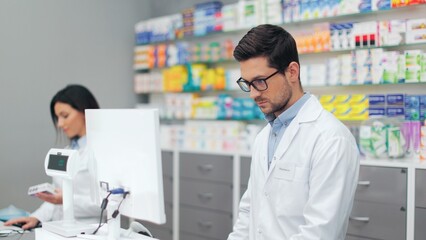 Pharmacists working with cash register. Two druggists in uniform standing near showcase with...