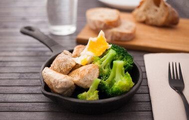 Ppieces of fried chicken breast with boiled broccoli and poached egg in cast iron portioned skillet