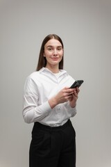 Naklejka premium Young Professional in a White Shirt Holds a Smartphone, Exuding Confidence and Engagement in a Minimalist Setting