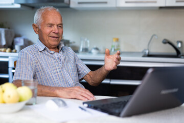 Retiree doing online shopping using laptop while sitting in the kitchen of home
