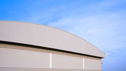 Warehouse factory industrial building with dome roof and louver ventilation on aluminum corrugated steel wall against blue sky background, low angle and perspective side view