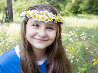 Portrait of a charming smiling girl of 12 years old in a wreath of daisies in the park. Enjoy the moment, positive intention, joyful summer mood. Teenage joys