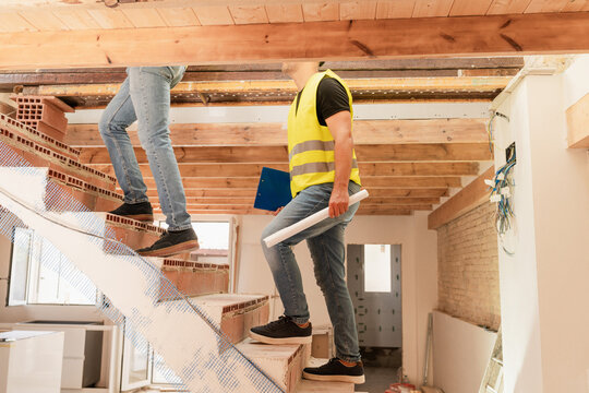 Two male Construction workers and engineer climbing brick staircase in building under construction - Powered by Adobe