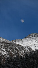 Half Moon on Blue Sky with Huge Snow Covered Mountain Rock  