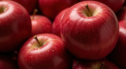 A close up shot showcasing a pile of vibrant red apples with visible stems and glossy surfaces nicely lit
