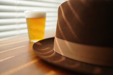 A close up of a brown fedora hat and a glass of beer, bathed in sunlight.