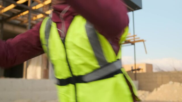 Wearing a hard hat and neon vest, a construction worker dances wildly on site, releasing pent up energy with fierce intensity. His chaotic movements explode into a burst of joy and total release.