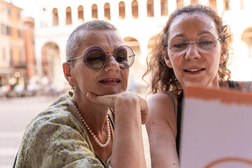 couple of middle aged female friends sitting at an outdoor coffee bar in a historic square looking at the menu