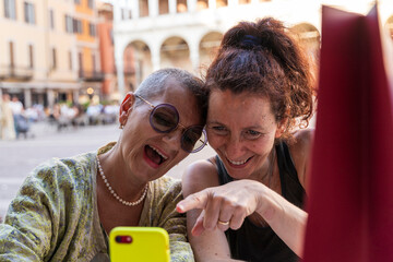 portrait of a beautiful couple of middle aged women on vacation having fun looking at cell phone sitting at a table outdoors