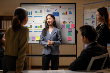 A woman is standing in front of a white board with a group of people
