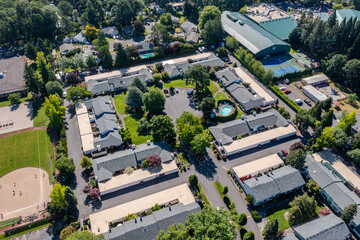 Aerial drone picture of a beautiful residential apartment complex in Cedar Mill, Portland, OR, captured at morning. Photo shows green courtyards, swimming pool, parking lots and housing buildings	
