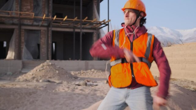 In front of a construction site, a foreman in a hard hat and vest dances with full intensity, arms moving in impulsive bursts. Driven by music, he moves with rhythm and effortless groove.