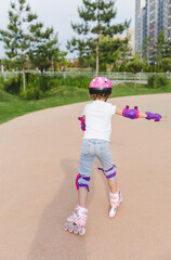 A little curly-haired girl rollerskates within the necessary facilities in the city. In a helmet...