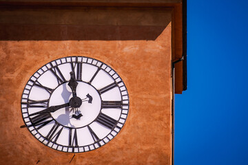 Detail of antique tower clock on textured orange wall against deep blue sky in Italy