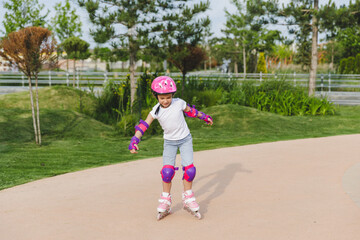 A little curly-haired girl rollerskates within the necessary facilities in the city. In a helmet...