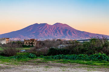 A breathtaking view of Mount Vesuvius during sunset, with soft orange and pink hues illuminating...