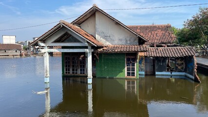A house stands damaged after being submerged in floodwaters. Muddy walls, debris, and broken parts show the impact of the flood and the hardship faced by the residents.