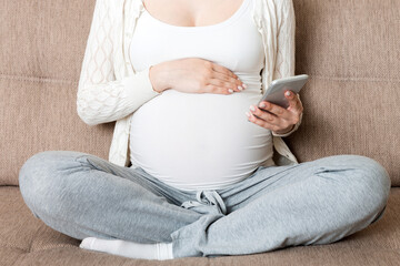 Caucasian pregnant girl using cellphone, resting on bed in home