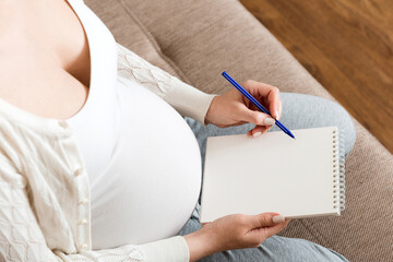 Pregnant woman makes notes. Concept of pregnancy, health care, medicine. Mother waiting of baby at the home